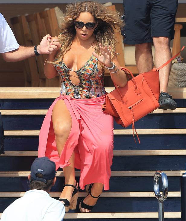 Mariah Carey steigt mit einer orangefarbenen Handtasche eine Treppe hinunter.