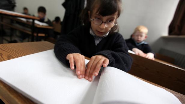 Ein Mädchen mit Brille liest ein Buch in Braille-Schrift.
