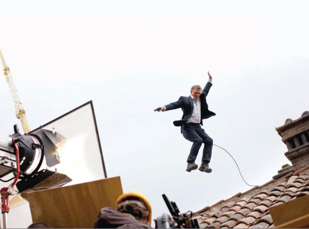 Daniel Craig springt als James Bond auf einem Dach in die Luft.