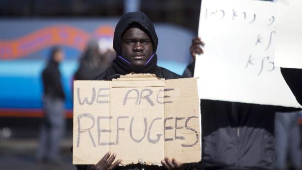 Ein junger Mann hält ein Schild mit der Aufschrift „We are refugees“.
