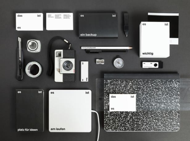 Eine Sammlung von Büroartikeln, darunter Notizbücher, Stifte, eine Kamera und ein USB-Stick, auf einem grauen Hintergrund.