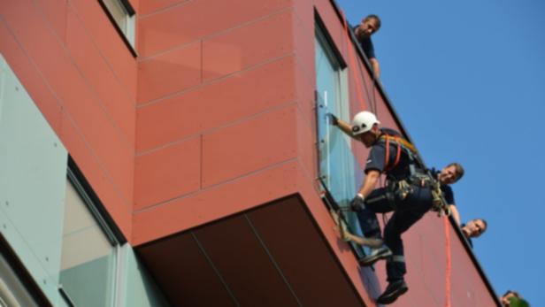 Ein Fensterputzer seilt sich an einem modernen Gebäude ab, während Kollegen ihn sichern.