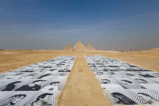 Eine Installation mit Porträtfotos vor den Pyramiden von Gizeh.