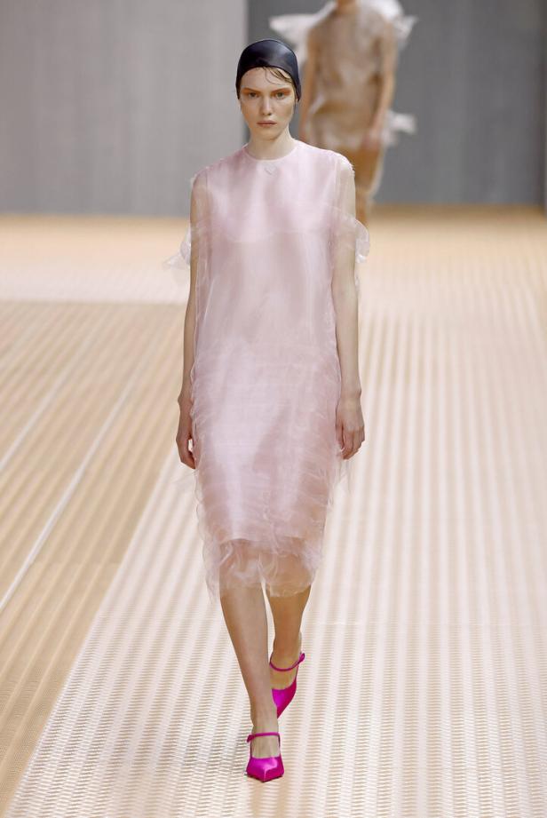 Eine Frau in einem transparenten, rosa Kleid und pinkfarbenen Schuhen auf einem Laufsteg.