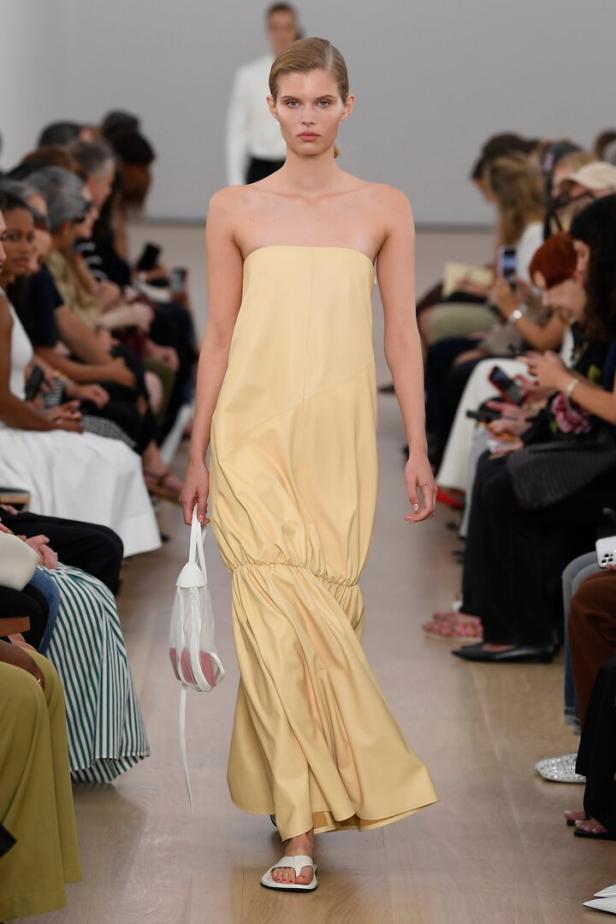Ein Model präsentiert ein trägerloses, hellgelbes Kleid auf einem Laufsteg.