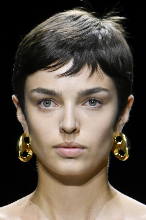 Porträt einer Frau mit kurzen, dunklen Haaren und goldenen Ohrringen.