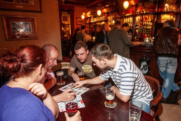 Eine Gruppe von Leuten sitzt in einem Pub und spielt ein Spiel bei Bier und Cocktails.