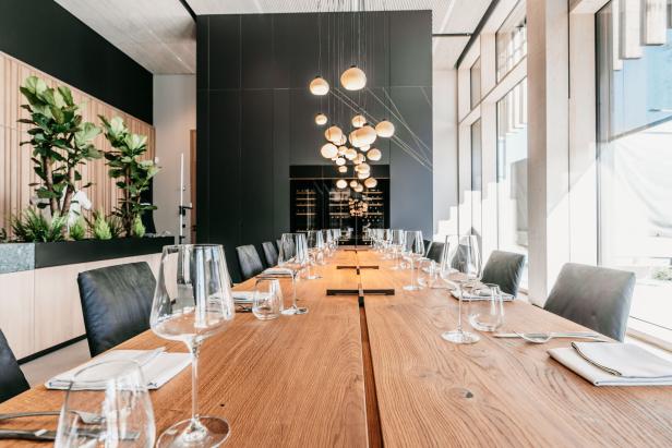 Ein langer Holztisch ist für ein formelles Abendessen mit Gläsern und Geschirr gedeckt.