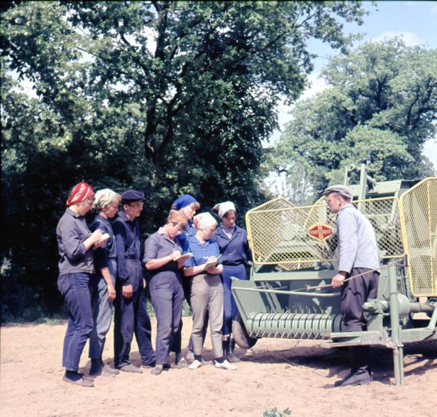 Eine Gruppe Landarbeiterinnen erhält eine Einweisung an einer Ballenpresse.