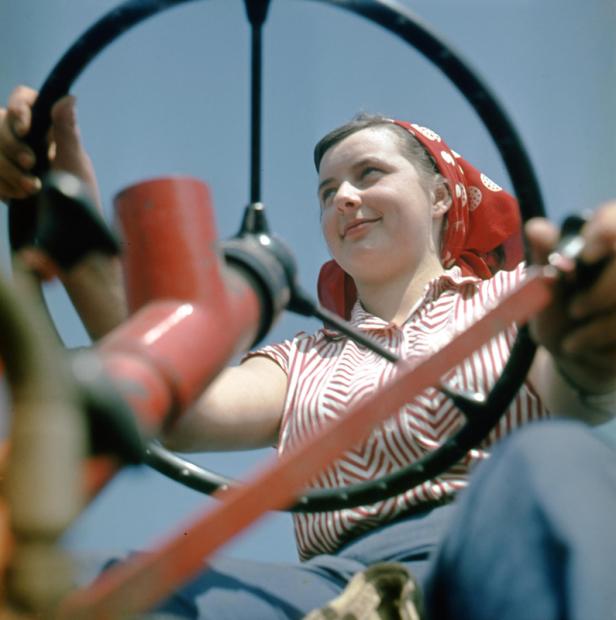 Eine junge Frau mit Kopftuch sitzt am Steuer eines Traktors.