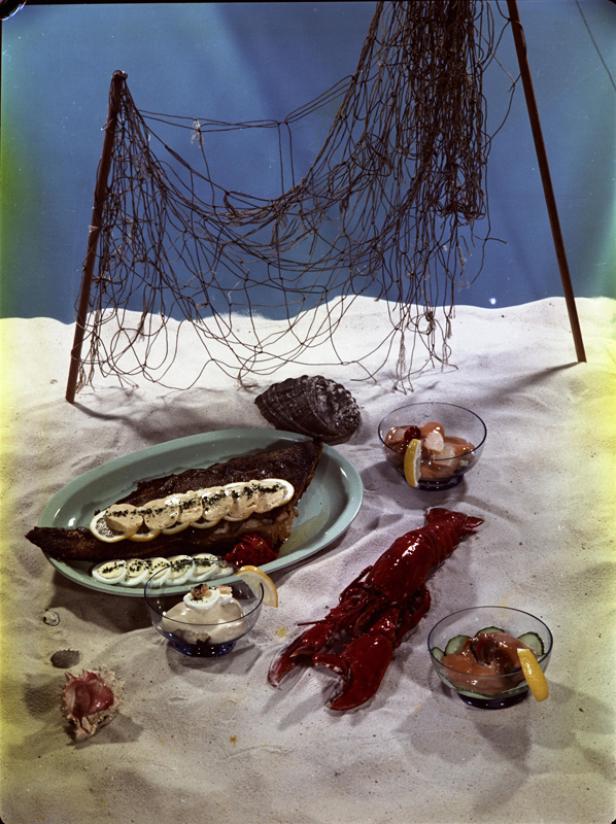 Ein Hummer, ein Fischgericht und verschiedene Vorspeisen sind auf Sand arrangiert.