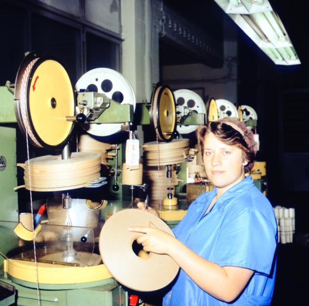 Eine Arbeiterin in einer Fabrik, die eine Spule in der Hand hält.