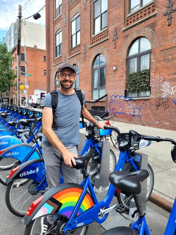 Mann in New York mit Leih-Fahrrad Citibikes mit LGBTQ Logo, Backsteingebäude im Hintergrund