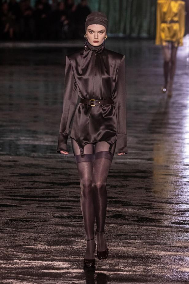 Eine Frau in einem braunen Satin-Kleid mit Strapsen auf dem Laufsteg.