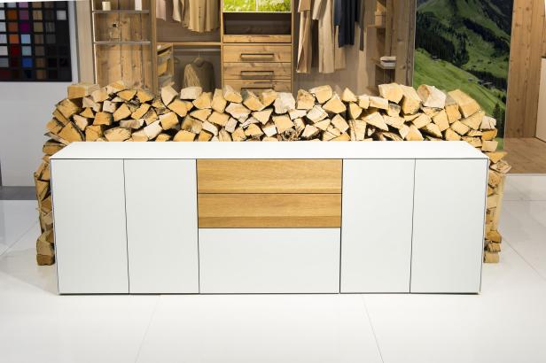 Ein weißes Sideboard mit Holzdetails steht vor einem Stapel Holzscheite.