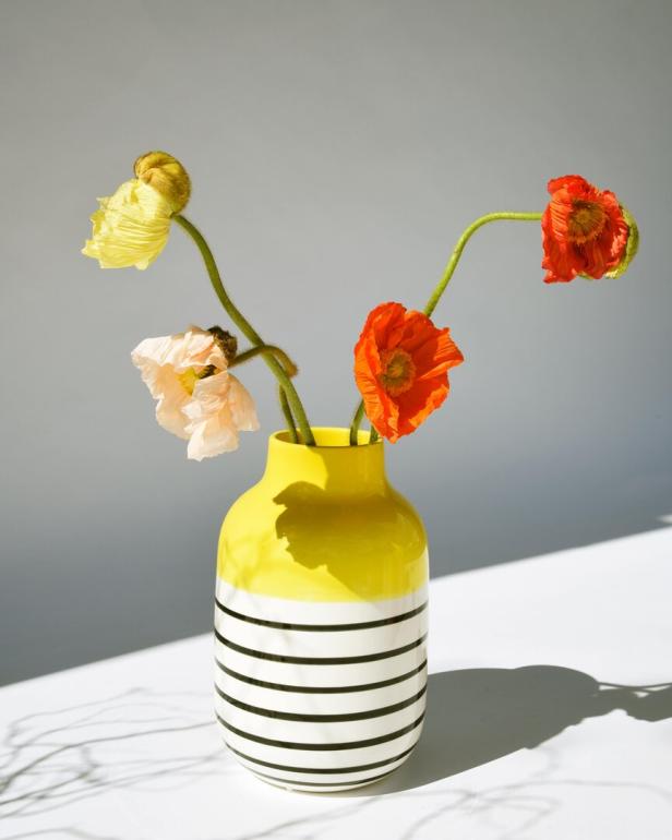 Mohnblumen in verschiedenen Farben stehen in einer gelb-weiß gestreiften Vase.