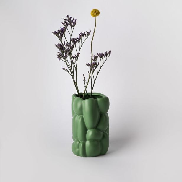 Trockenblumen und eine gelbe Kugelblume in einer grünen Vase.