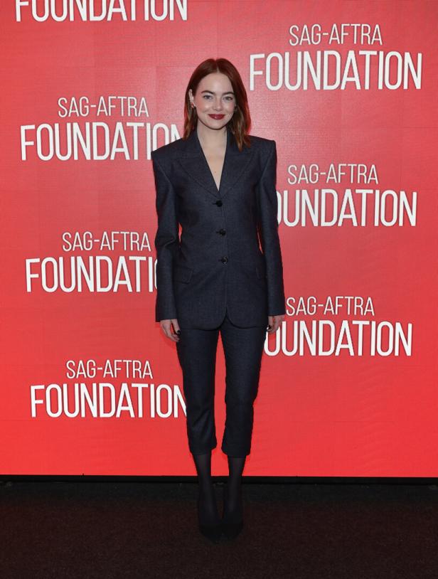 Emma Stone posiert vor einem roten Hintergrund mit dem Logo der SAG-AFTRA Foundation.