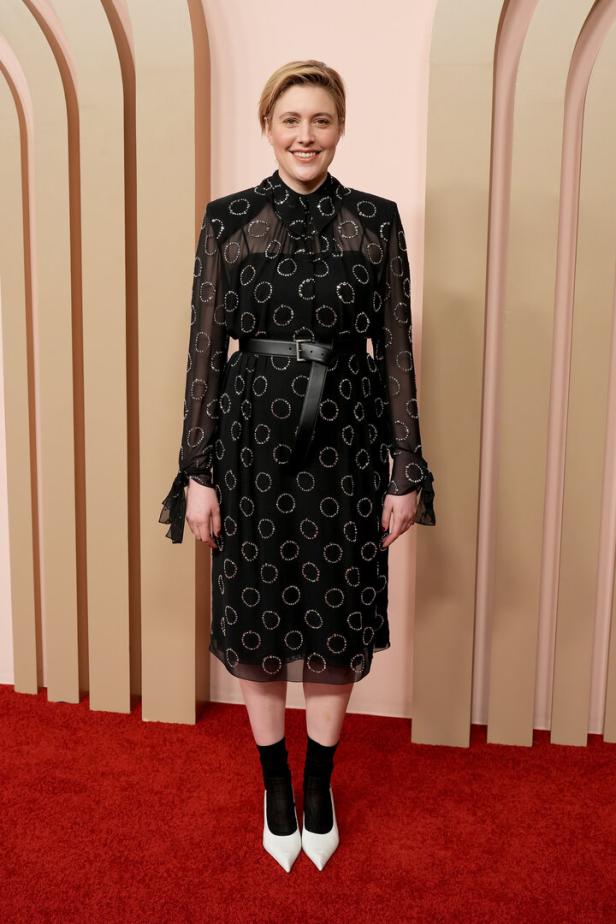 Greta Gerwig trägt ein schwarzes Kleid mit weißen Punkten und einen Gürtel.