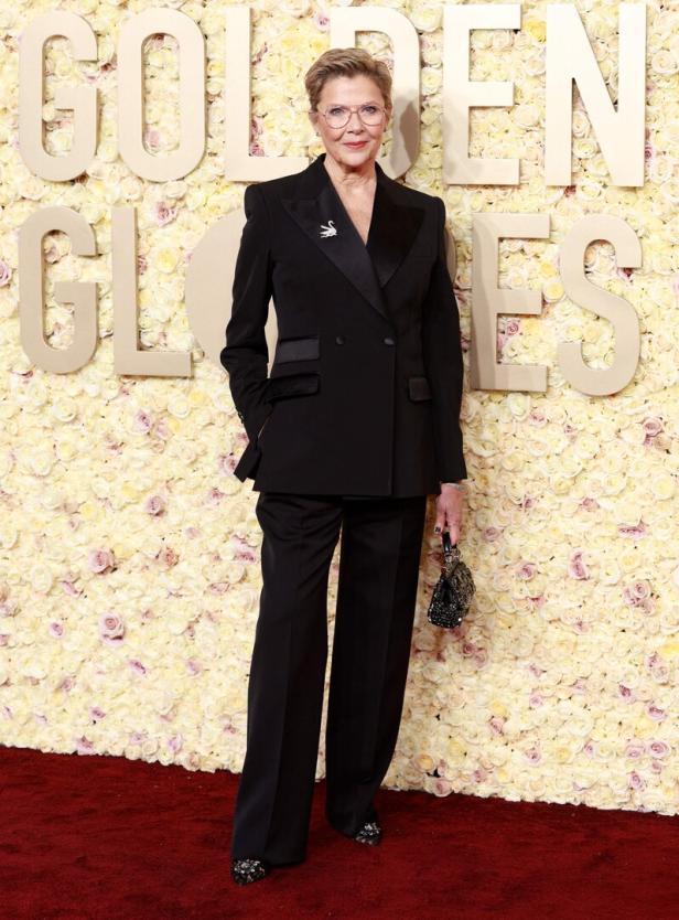 Eine Frau in einem schwarzen Hosenanzug posiert vor einer Wand mit Rosen und dem Schriftzug „Golden Globes“.