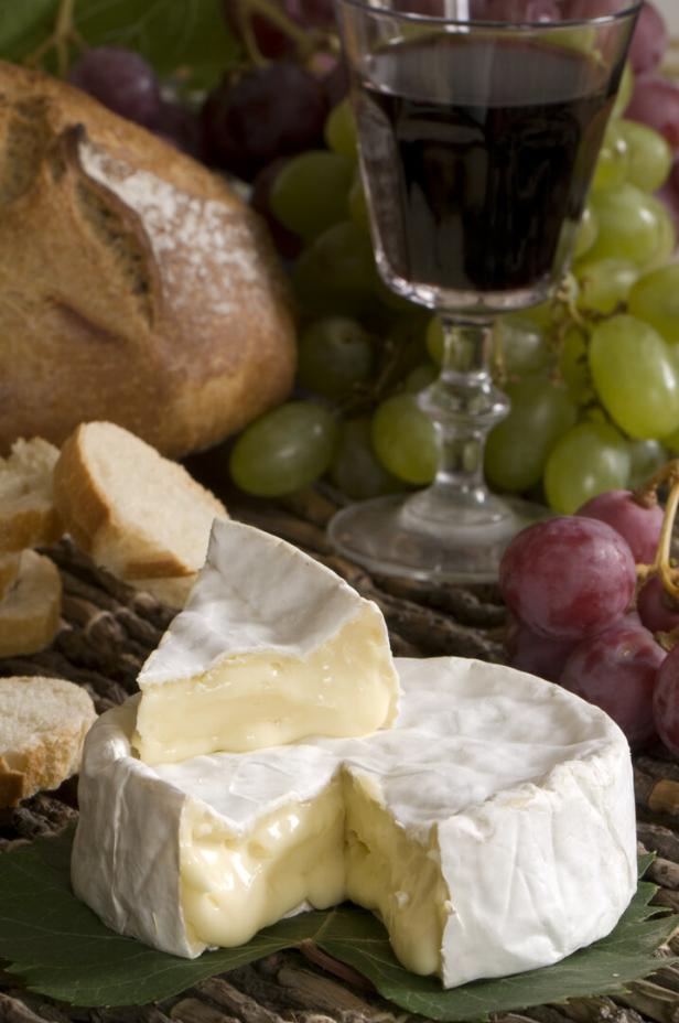Ein Camembert mit Brot, Trauben und einem Glas Rotwein auf einem Tisch.