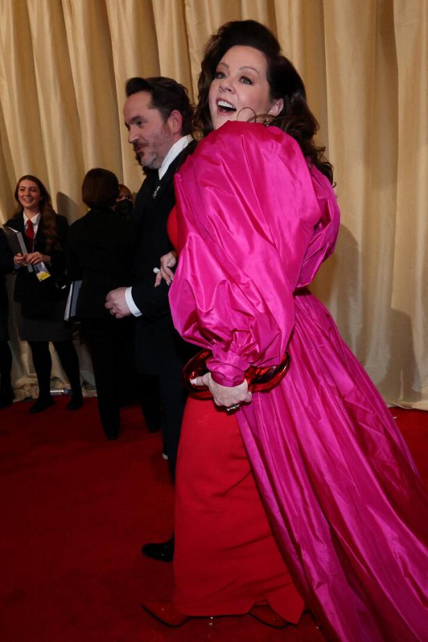 Melissa McCarthy in einem auffälligen pinkfarbenen Kleid auf einem roten Teppich.