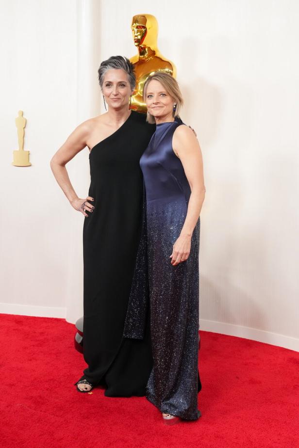 Jodie Foster und Alexandra Hedison posieren auf dem roten Teppich vor einer Oscar-Statue.