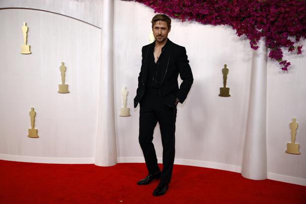 Ryan Gosling posiert auf dem roten Teppich vor einer Wand mit Oscar-Statuetten.