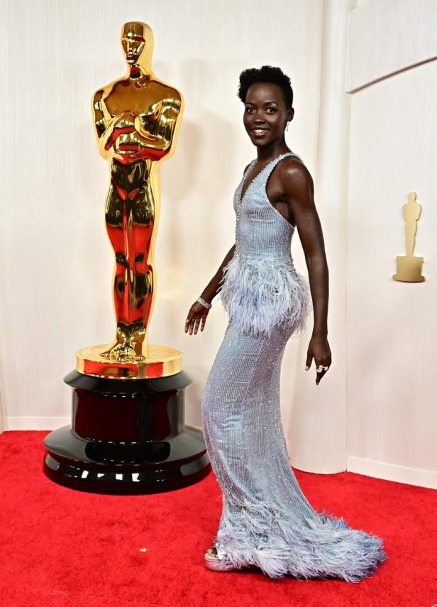 Lupita Nyong'o posiert auf dem roten Teppich neben einer Oscar-Statue.