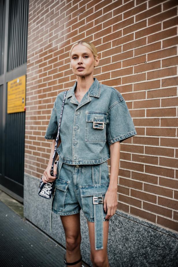 Eine Frau in einem Jeans-Outfit von Fendi posiert vor einer Backsteinmauer.