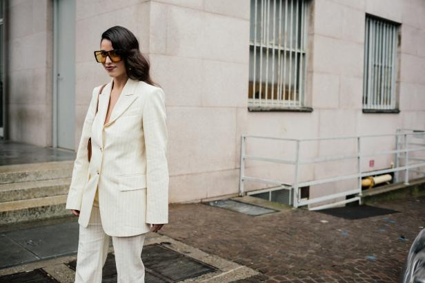 Eine Frau mit Sonnenbrille trägt einen weißen Anzug mit Nadelstreifen.