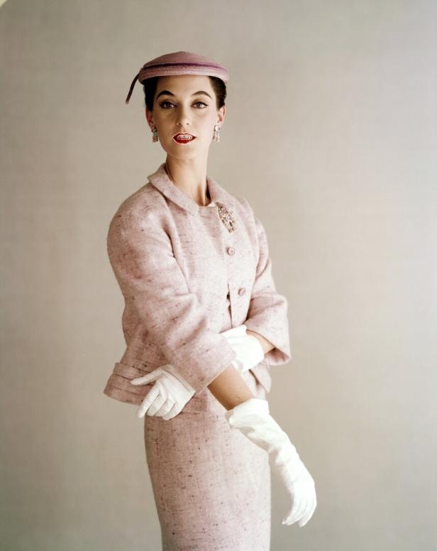 Eine Frau in einem rosa Tweed-Kostüm mit Hut und weißen Handschuhen.