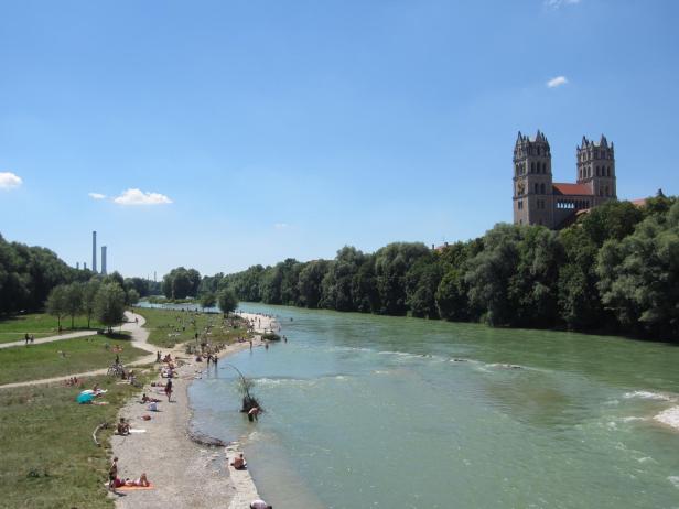 Menschen entspannen an der Isar in München mit Blick auf die St.-Maximilians-Kirche.