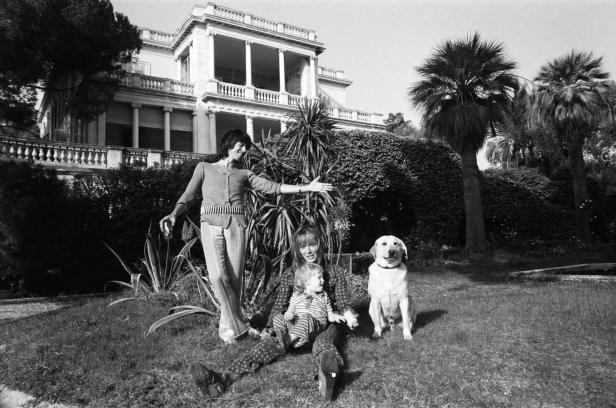 Ein Schwarzweißfoto von Keith Richards mit Familie und Hund vor einem großen Haus.