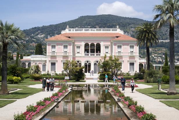 Die Villa Ephrussi de Rothschild, ein rosafarbenes Herrenhaus mit Garten und Teich, wird von Besuchern erkundet.