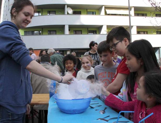 Eine Frau gießt eine rauchende Flüssigkeit in eine Schüssel, umgeben von Kindern.