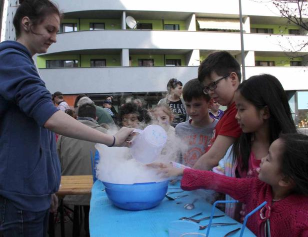 Eine Frau gießt eine Flüssigkeit in eine Schüssel mit Trockeneis, umgeben von Kindern.