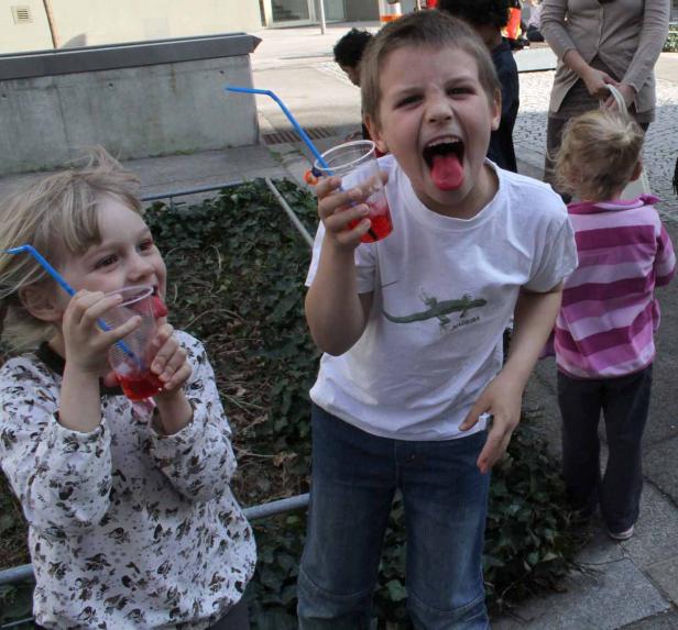 Zwei Kinder trinken rote Limonade mit blauen Strohhalmen.