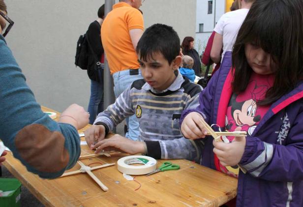 Zwei Kinder basteln an einem Holztisch mit Stöcken und Klebeband.
