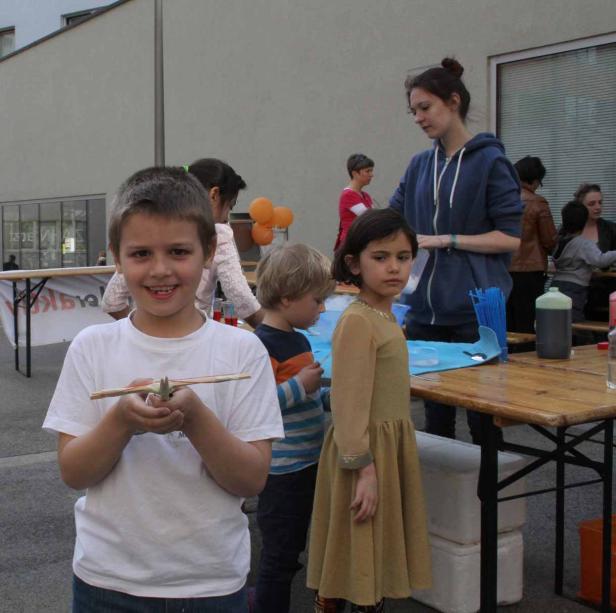 Ein lächelnder Junge hält ein kleines Flugzeug in den Händen, umgeben von anderen Kindern und einer Frau.