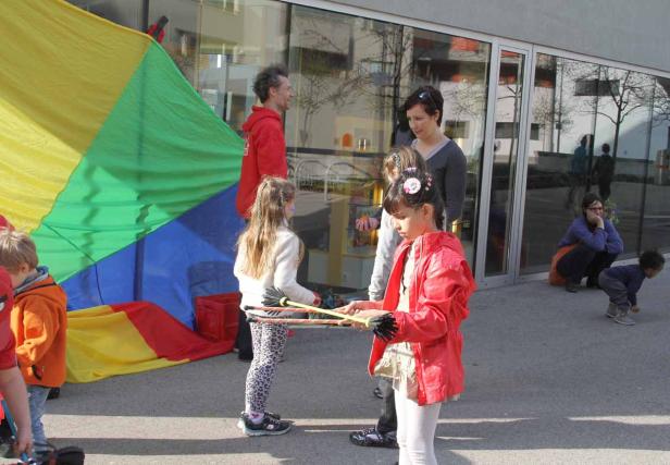 Kinder spielen mit einem bunten Schwungtuch und Hula-Hoop-Reifen im Freien.