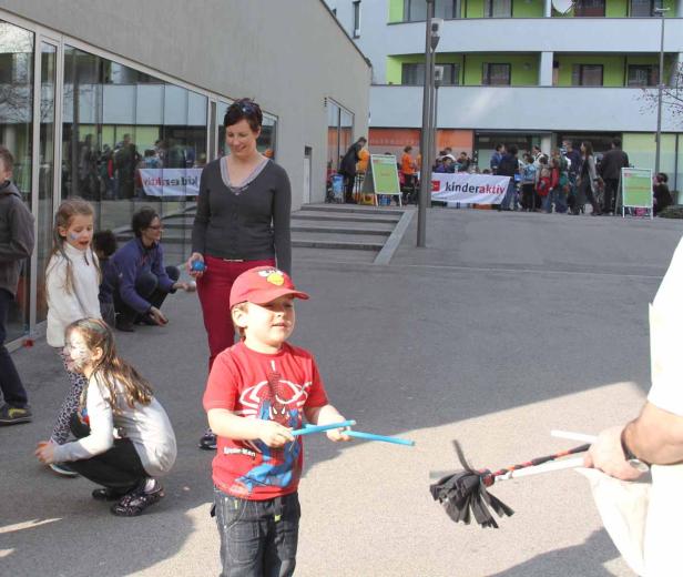 Ein Junge mit Spiderman-T-Shirt spielt mit Jonglierstäben vor einem Gebäude, wo eine Kinderveranstaltung stattfindet.