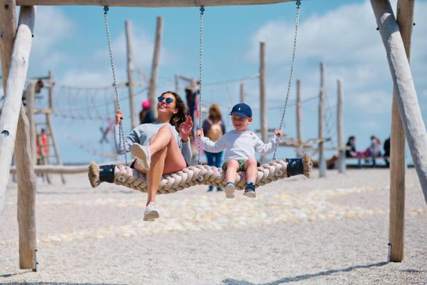 Eine Frau und ihr Sohn sitzen auf einer Schaukel am Spielplatz und lachen.