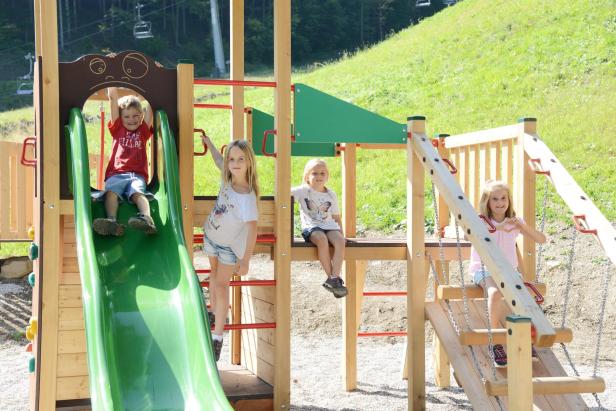 Eine Gruppe Kinder spielt auf einem hölzernen Spielplatz im Freien.