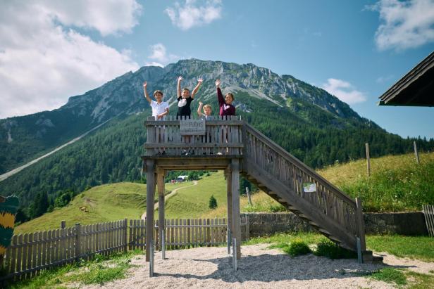 Vier Kinder stehen auf einem Holzdeck und winken.