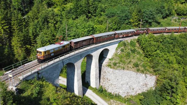 Ein Zug überquert eine Brücke, während er durch eine malerische Berglandschaft fährt.