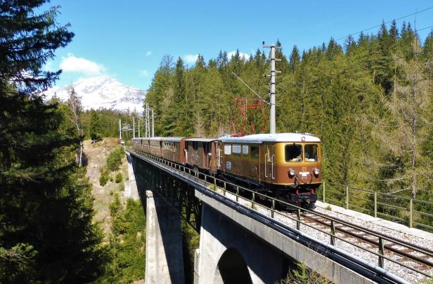 Ein Zug überquert eine Brücke, während er durch eine malerische Berg- und Waldlandschaft fährt.