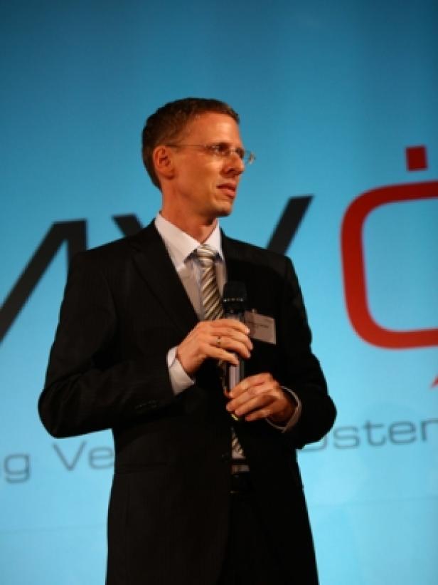 Ein Mann mit Brille und Anzug spricht bei einer Präsentation ins Mikrofon.