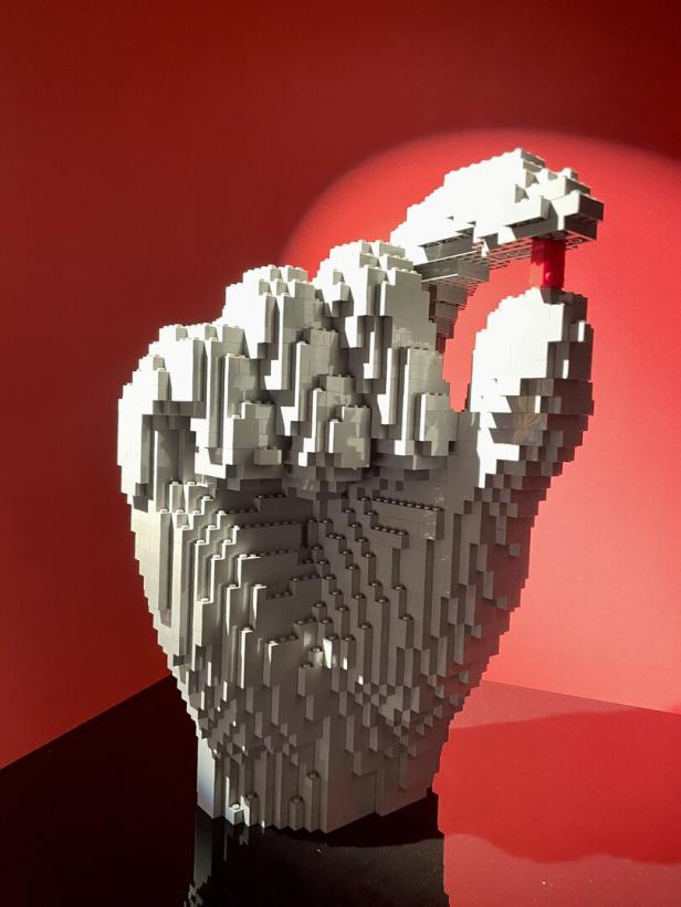 Eine graue Hand aus Legosteinen hält einen einzelnen roten Legostein.