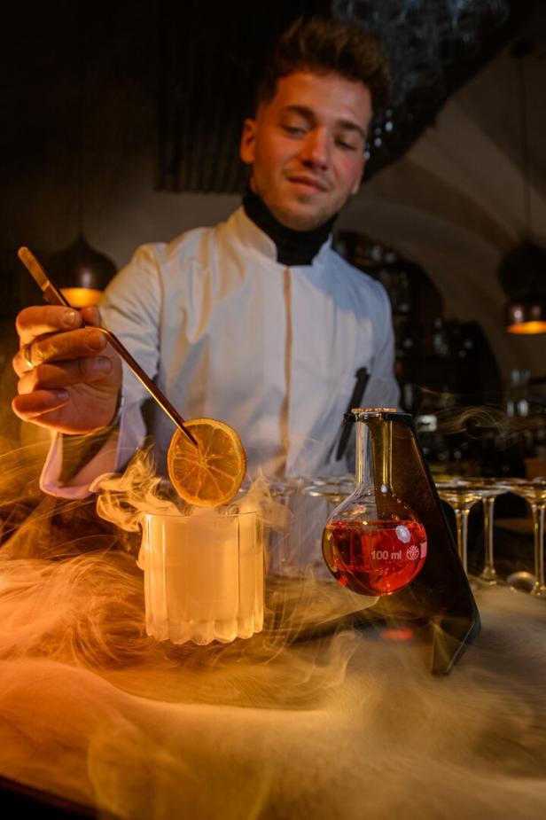 Ein Barkeeper garniert einen Cocktail mit einer Orangenscheibe, umgeben von Trockeneisnebel.